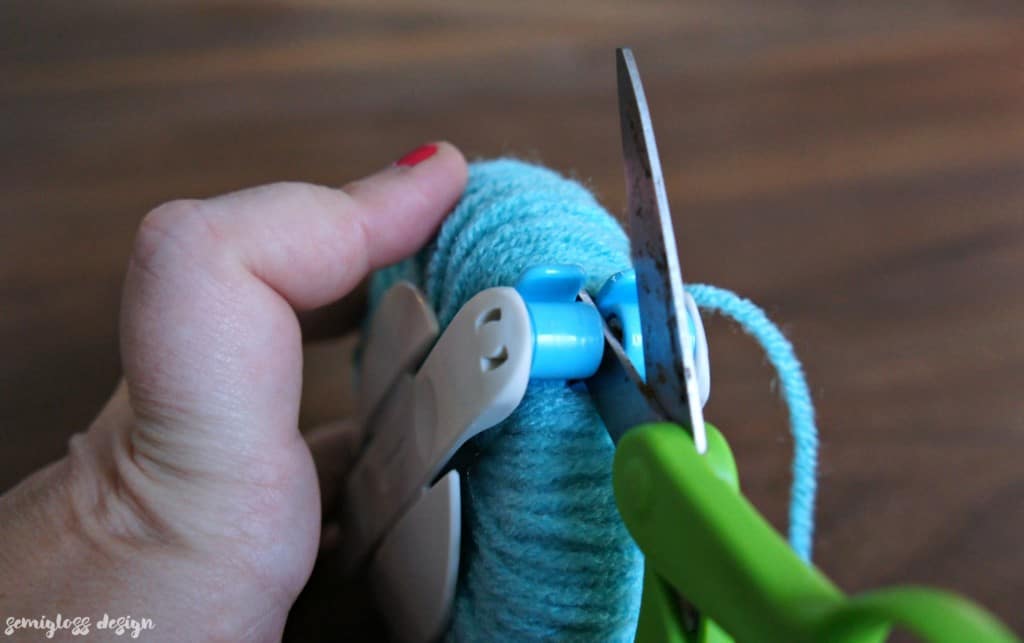 Cut the yarn on the pom pom maker