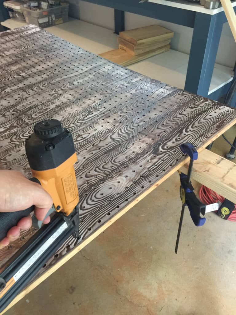 Using a nail gun to attach pegboard panel to the wood frame