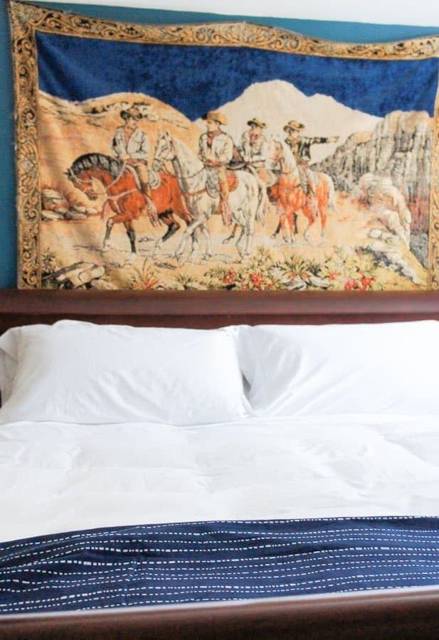 white sheets and vintage tapestry on wall