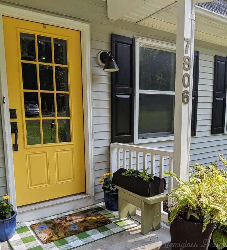 front porch makeover featuring yellow front porch, layered rugs, toolbox planter and potted daisies. 