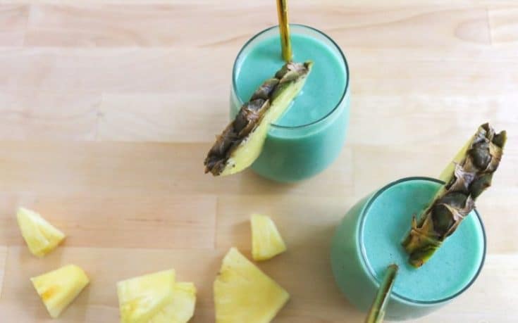 frozen blue Hawaiian cocktail in glasses with pineapple chunks scattered nearby