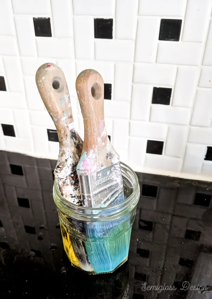 two brushes soaking in jar to remove paint