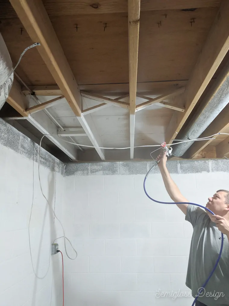 man spraying paint on exposed ceiling in basement