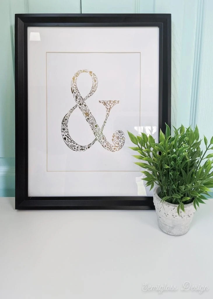 gold foil ampersand art in frame with plant