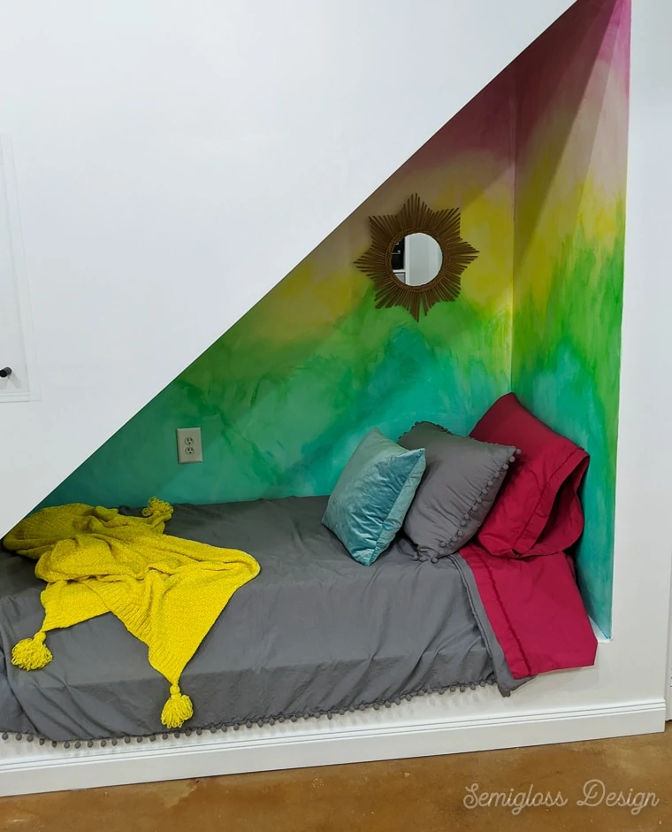 sleeping area under stairs with rainbow mural