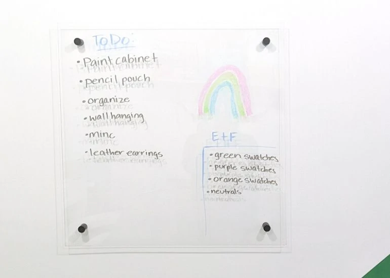 clear dry erase board on wall with to do list and rainbow drawing