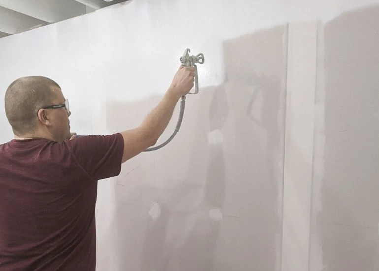 man using paint sprayer on walls