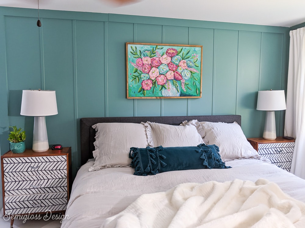 bed with gray bedding against teal walls with floral painting