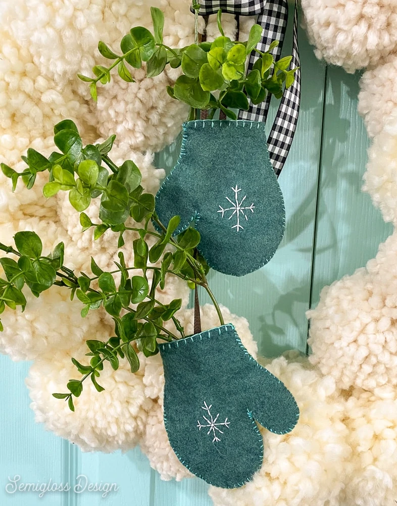 adding greenery to felt mitten on pom pom wreath