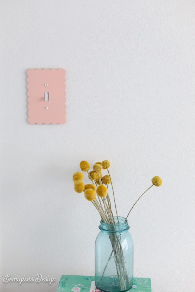 pink scalloped light switch cover with vase of dried flowers