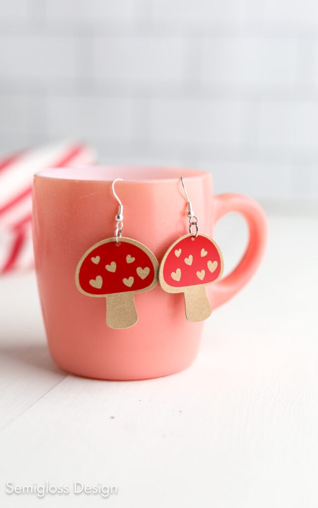 mushroom earrings made of faux leather hanging on pink mug