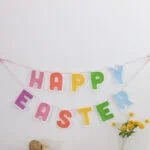 easter banner made of felt over table with vase of flowers and wicker snail