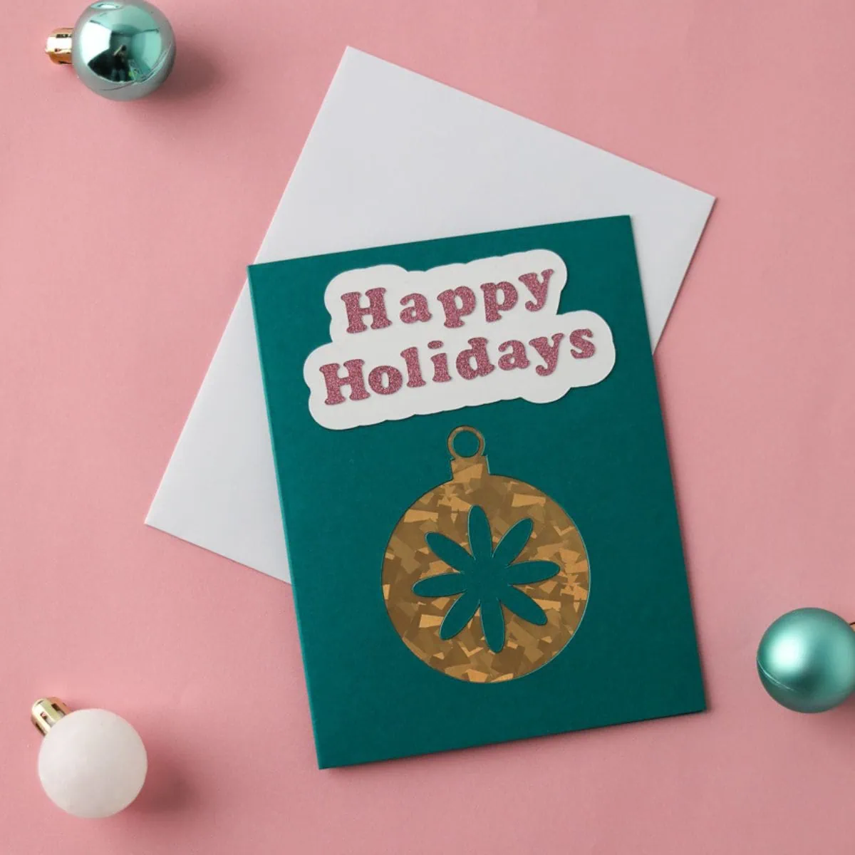 Teal cutaway card with gold ornament and glitter lettering that says Happy Holidays.