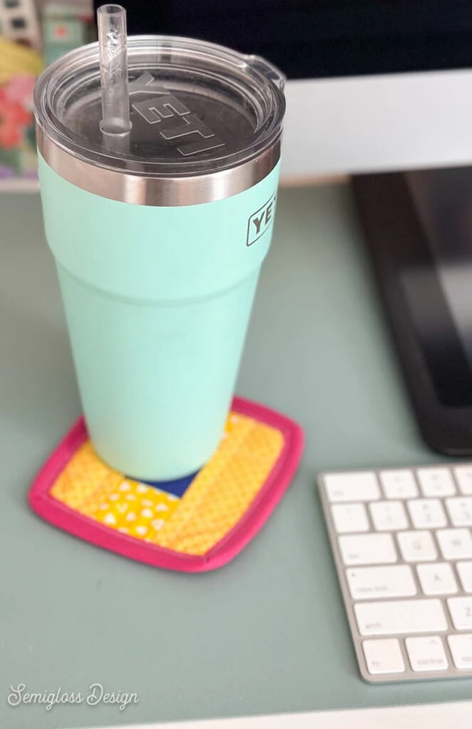 aqua cup sitting on yellow, blue and pink coaster on desk. 